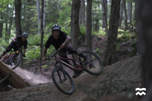 Deux hommes en descente dans un sentier au Wolf Bike Park, légèrement de côté à cause de la vitesse